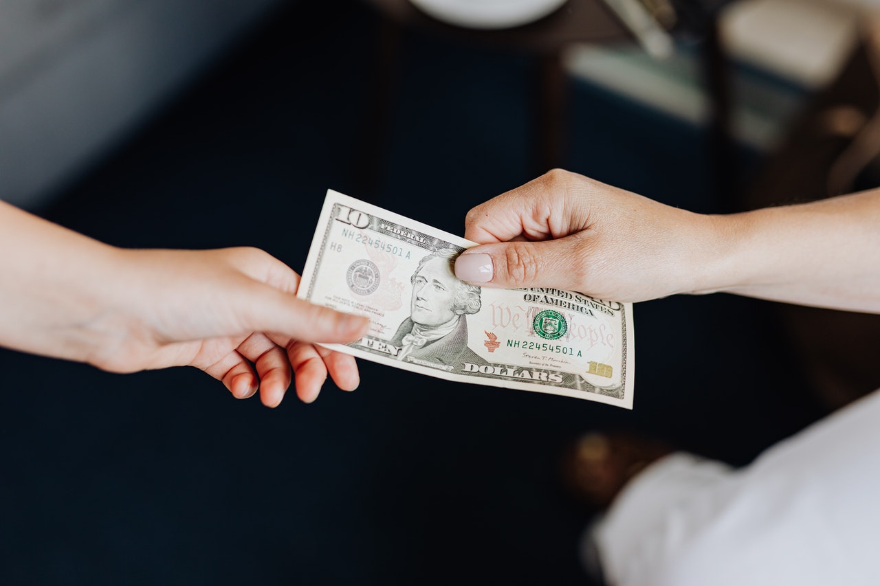 Close-up of two hands exchanging a ten-dollar bill against a dark, blurred indoor setting